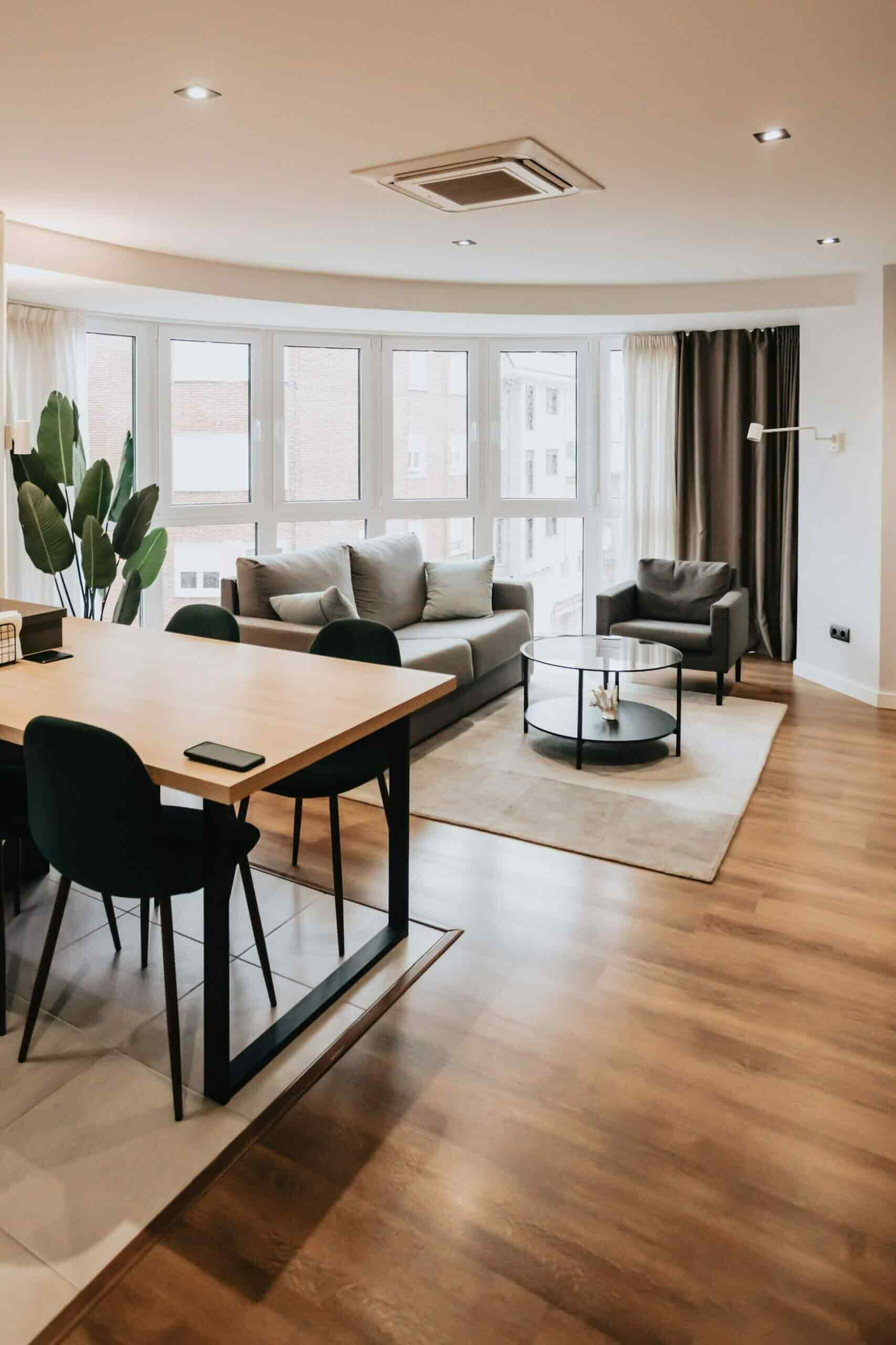 Open-plan dining and living area with wood table, black chairs, and floor-to-ceiling windows
